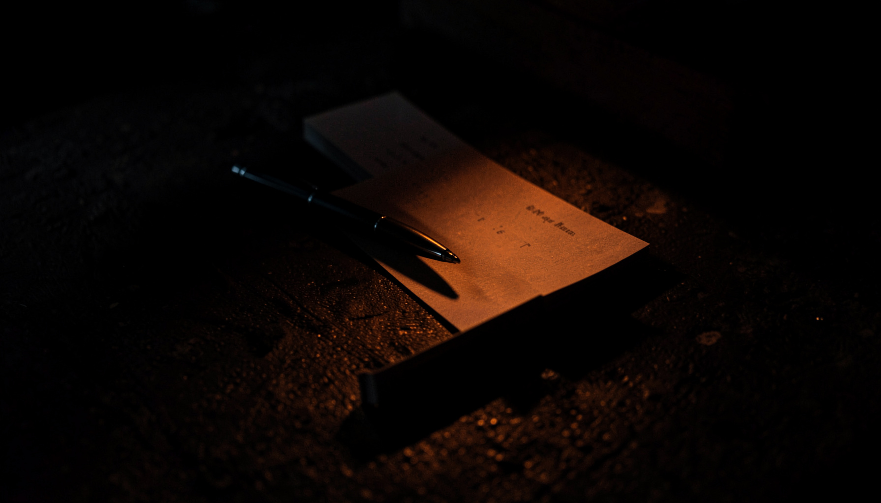 A moody low-light image of stacked business cards and a pen resting on a dark textured surface.