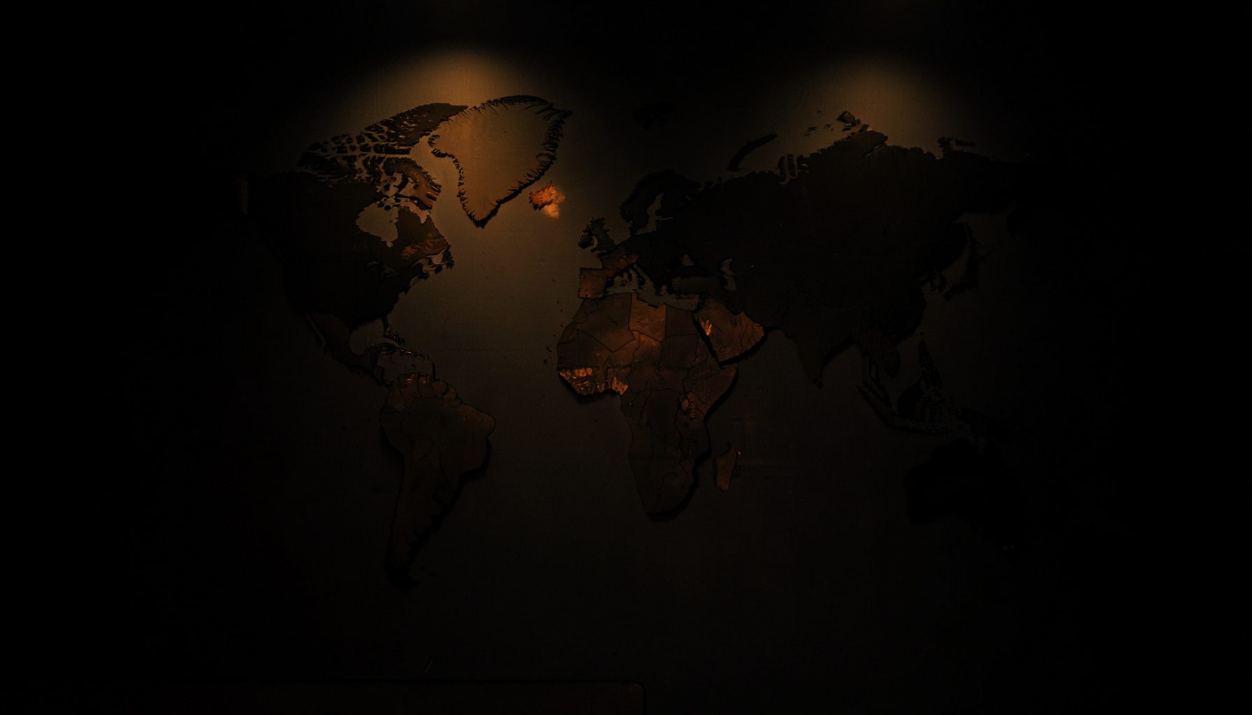 A quiet dark photograph of a wall-mounted world map with soft amber spotlight accents.