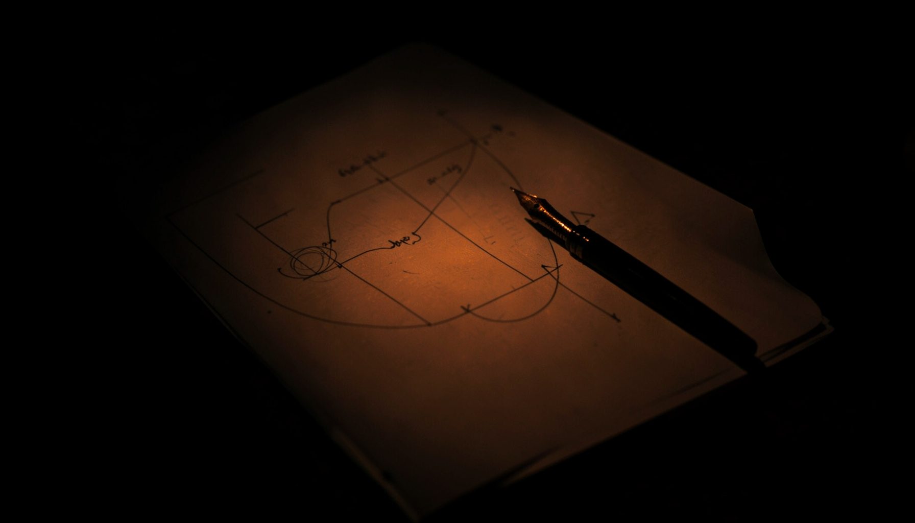 A dark low-key photograph of a notebook open to a hand-drawn plan with a fountain pen beside it.